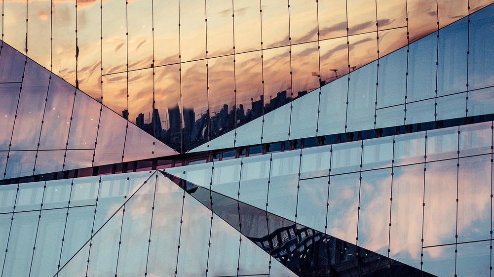 Immeuble avec façade en verre reflétant une vue urbaine au coucher du soleil.